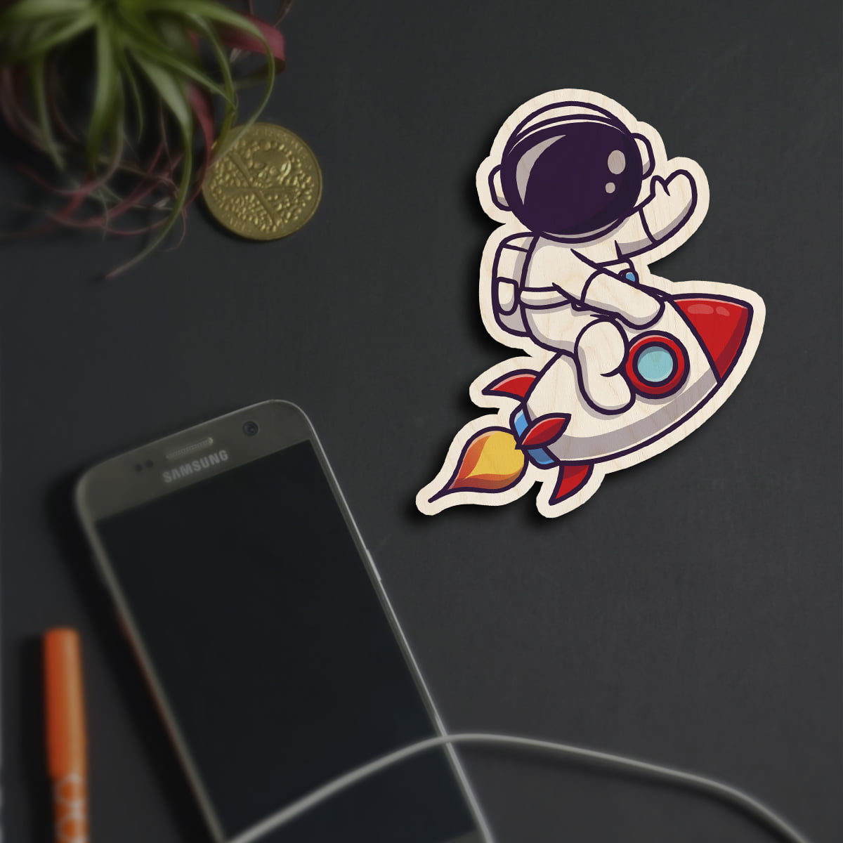 Alternate angle on the kids fridge magnet, showing cartoon astronaut on red rocket with flame trail, in birch wood.