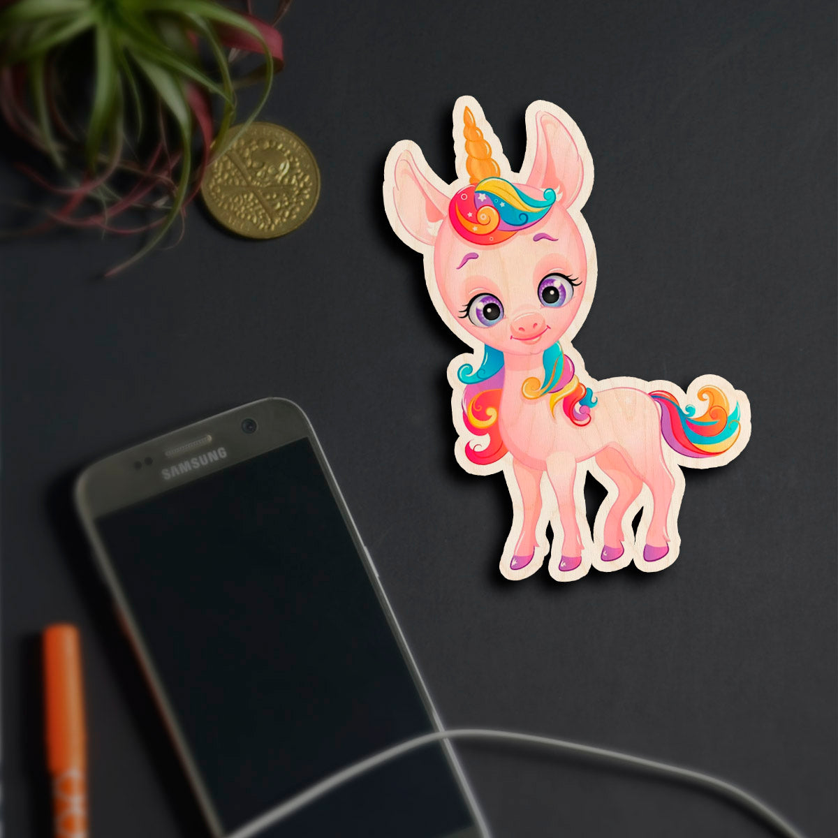 Alternate angle on the kids fridge magnet, showing cartoon unicorn silhouette with rainbow mane and tail, in birch wood.