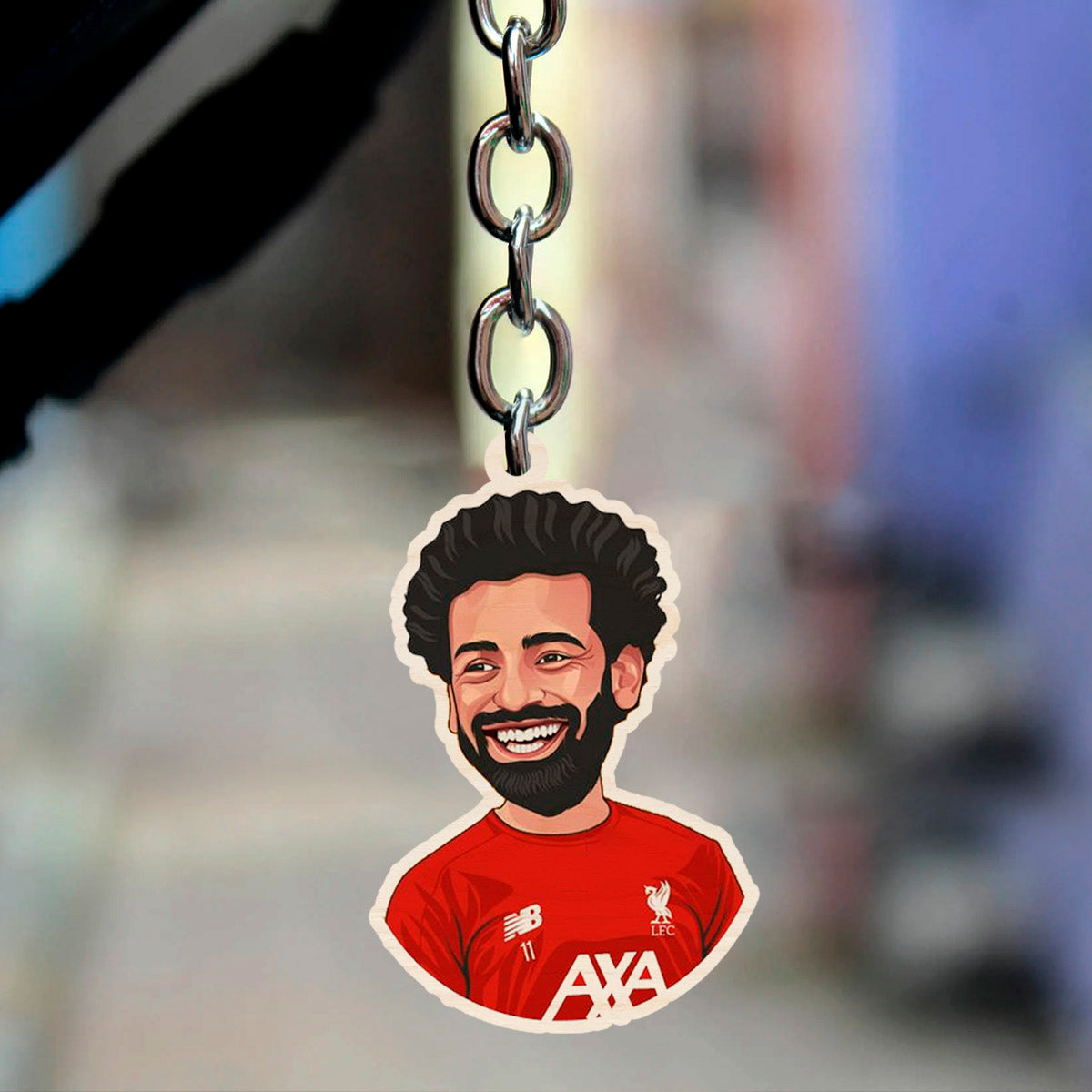 Alternate angle on the wooden keychain, showing salah caricature with signature curls in the 2021-22, on neutral backdrop.