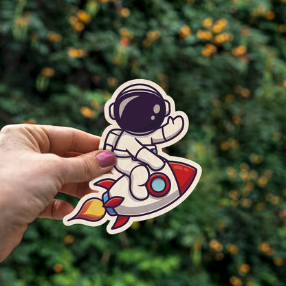 Detail crop of the kids fridge magnet, with cartoon astronaut on red rocket with flame trail, on birch wood face.
