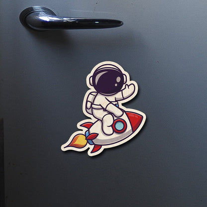 On-fridge lifestyle shot of the kids fridge magnet, showing cartoon astronaut on red rocket with flame trail.