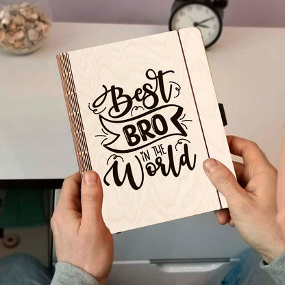 Detail crop on the wooden notebook cover, with hand-lettered brother-tribute script with ribbon banner, sharp birch grain.