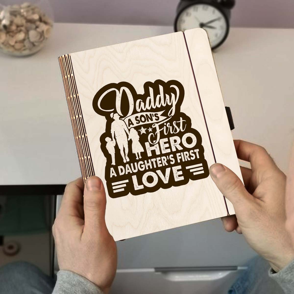 Detail crop on the wooden notebook cover, with father-and-children silhouette plus 'Daddy first hero /, sharp birch grain.