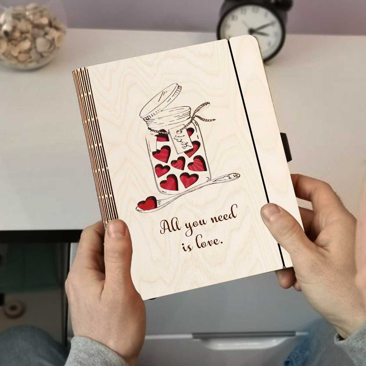 Detail crop on the wooden notebook cover, with mason jar with red hearts + 'All You Need Is Love' cursive.