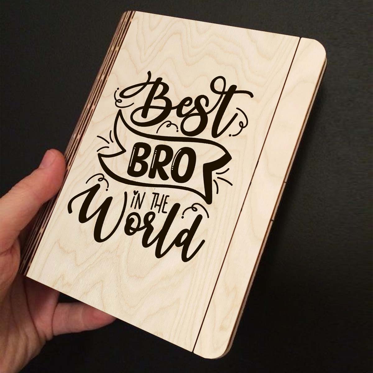 Open spread of the wooden notebook, with hand-lettered brother-tribute script with ribbon banner, and ruled inner pages.
