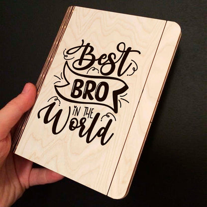 Open spread of the wooden notebook, with hand-lettered brother-tribute script with ribbon banner, and ruled inner pages.