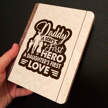 Open spread of the wooden notebook, with father-and-children silhouette plus 'Daddy first hero /, and ruled inner pages.