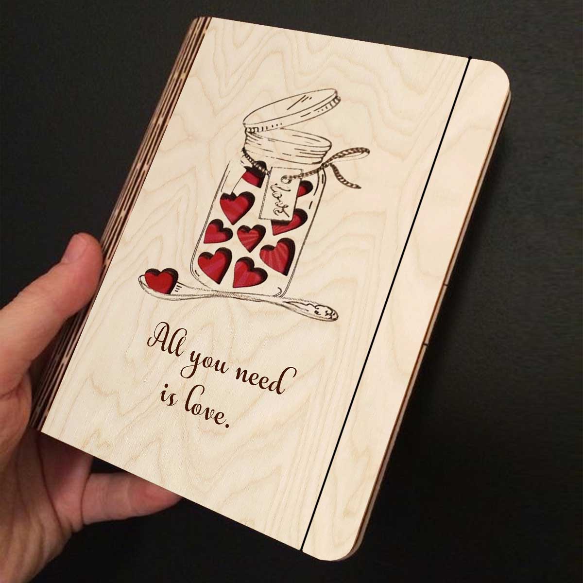 Open spread of the wooden notebook, with mason jar with red hearts + 'All You Need Is Love' cursive, and ruled inner pages.