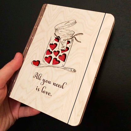 Open spread of the wooden notebook, with mason jar with red hearts + 'All You Need Is Love' cursive, and ruled inner pages.