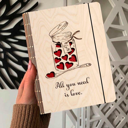 Alternate angle on the wooden notebook, showing mason jar with red hearts + 'All You Need Is Love' cursive, in birch wood.