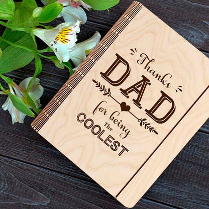 Wooden notebook cover on a clean backdrop showing thanks DAD' typography with heart-arrow vines, on a 21x17 cm birch wood.