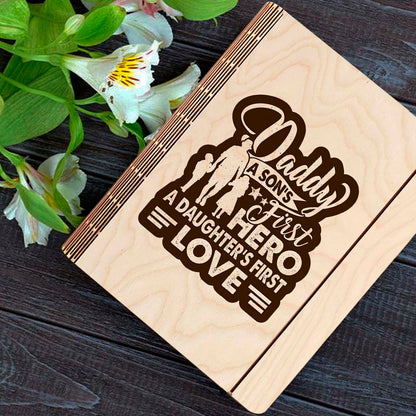 Wooden notebook cover on a clean backdrop showing father-and-children silhouette plus 'Daddy first hero /.