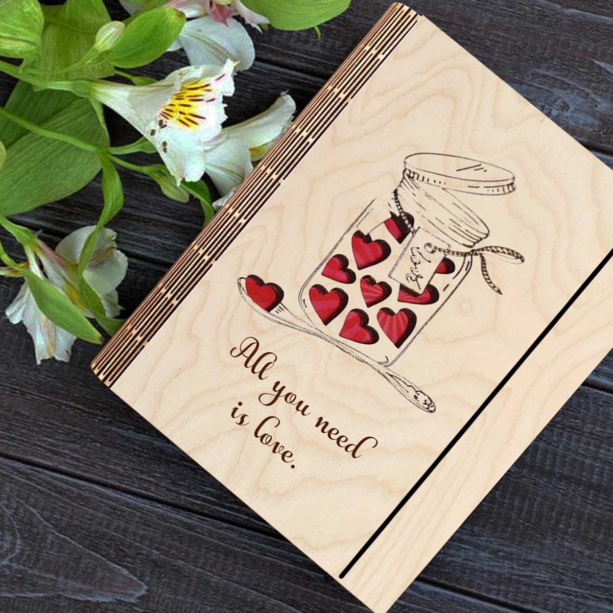 Wooden notebook cover on a clean backdrop showing mason jar with red hearts + 'All You Need Is Love' cursive.