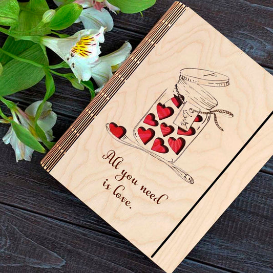 Wooden notebook cover on a clean backdrop showing mason jar with red hearts + 'All You Need Is Love' cursive.