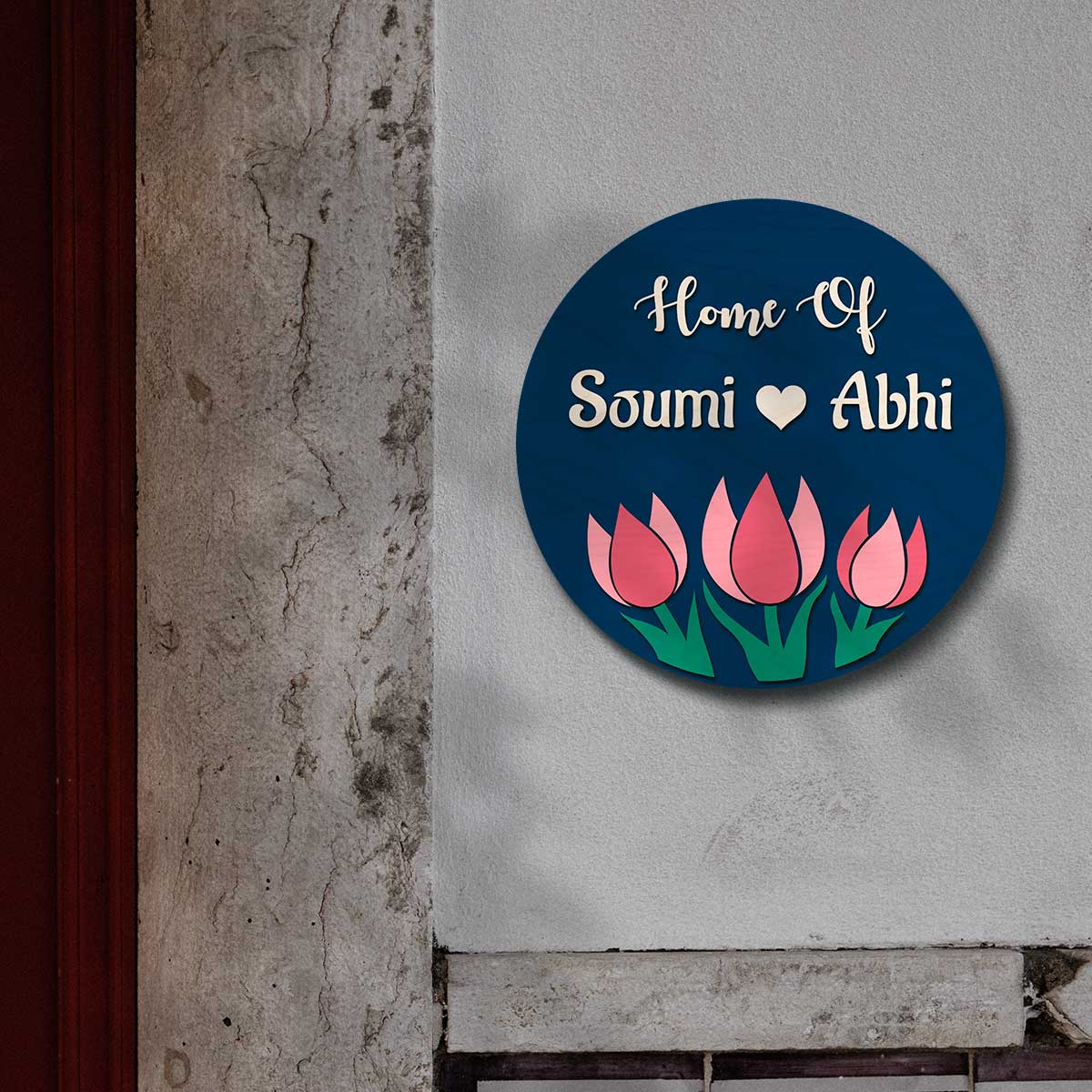 Close-up of three raised pink tulips and green leaves on the navy wooden nameplate