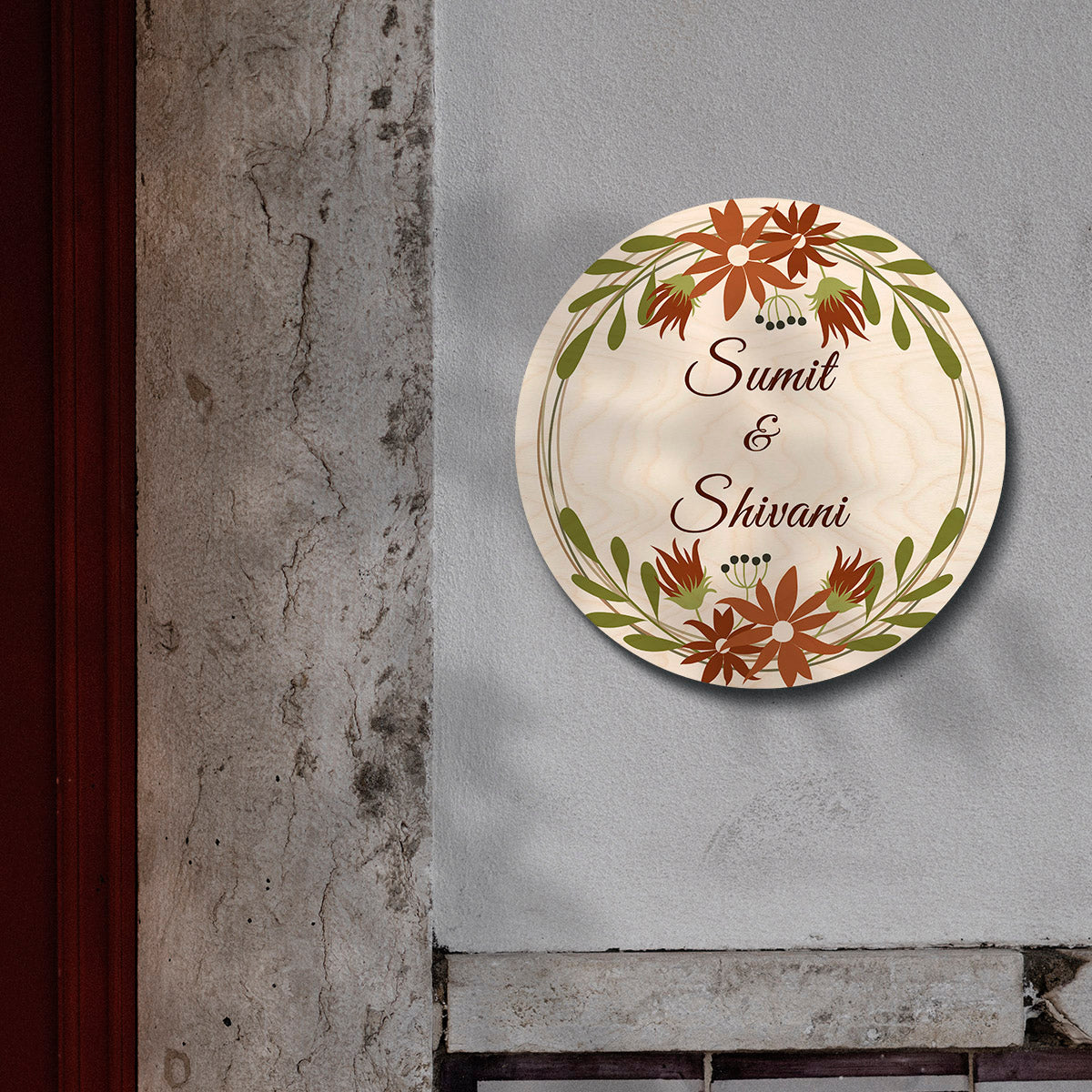 Couple names in script inside rust-orange wreath on floral round name board