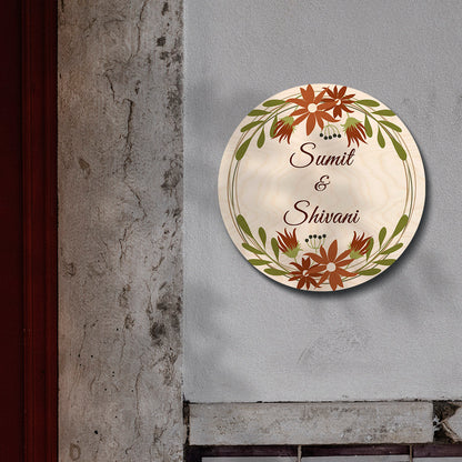 Couple names in script inside rust-orange wreath on floral round name board