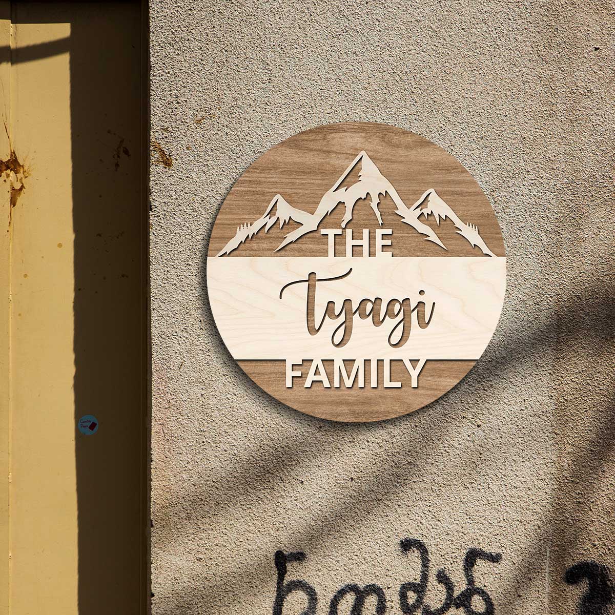Round nature-themed family name plate on a wall with THE, surname and FAMILY lettering