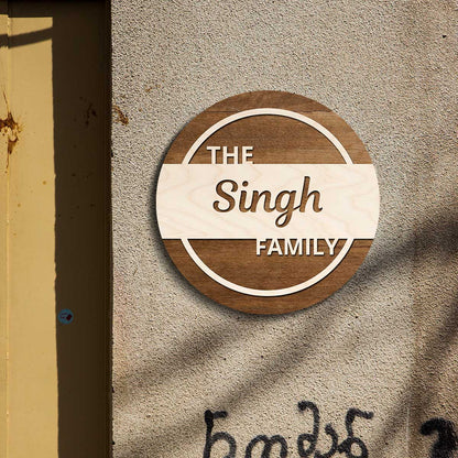 Round two-tone wooden family name plate on a wall with THE and FAMILY lettering